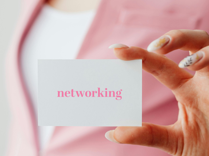 women in pink blazer, pink background, holding up a card that reads: networking